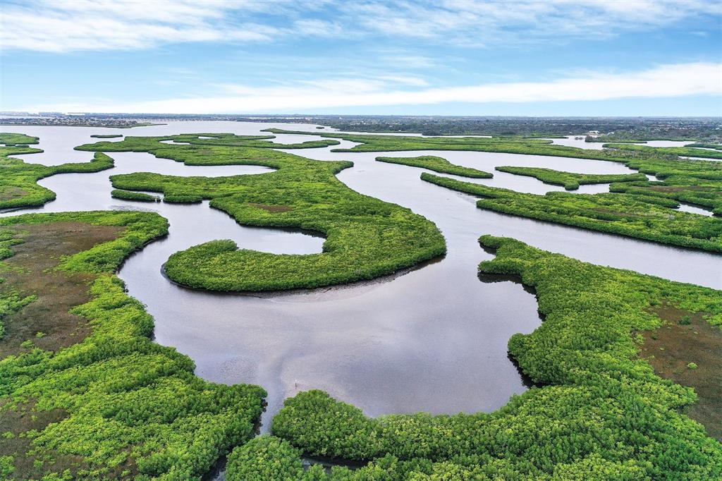 An aerial view shows a winding waterway surrounded by dense green mangrove islands and vegetation — 7803 GRAND ESTUARY TRAIL UNIT 208, BRADENTON, FL
