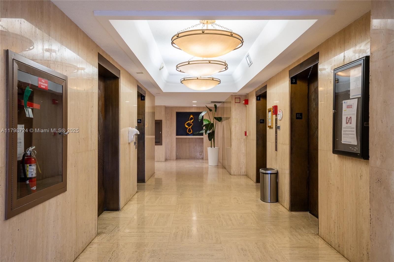 An elevator lobby features marble walls, tiled floors, three pendant lights, and a potted plant — 500 Three Islands Blvd # 801, Hallandale Beach FL 33009, HALLANDALE BEACH, FL