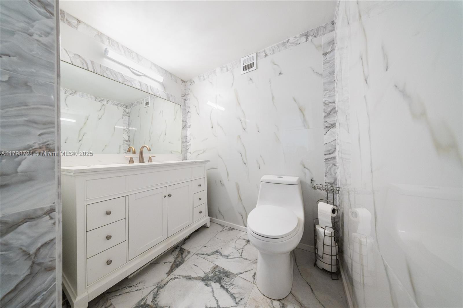 A bathroom features a white vanity, a toilet, and white marble-patterned tile walls and floors — 500 Three Islands Blvd # 801, Hallandale Beach FL 33009, HALLANDALE BEACH, FL
