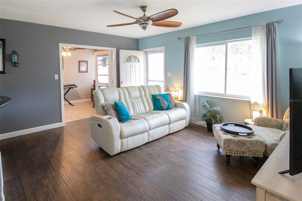 A living room features dark wood flooring, a white reclining sofa, and a light blue wall — 1725 BRADSHAW LANE N, ST PETERSBURG, FL