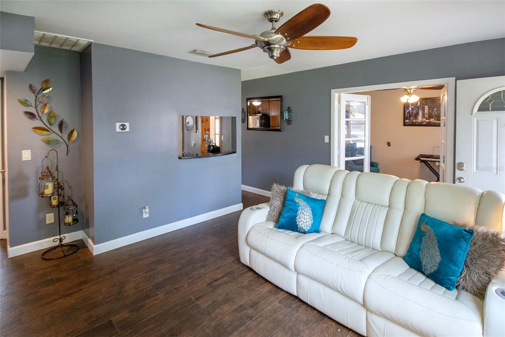 A living room features gray walls, wood-look flooring, a white sofa, and a ceiling fan — 1725 BRADSHAW LANE N, ST PETERSBURG, FL