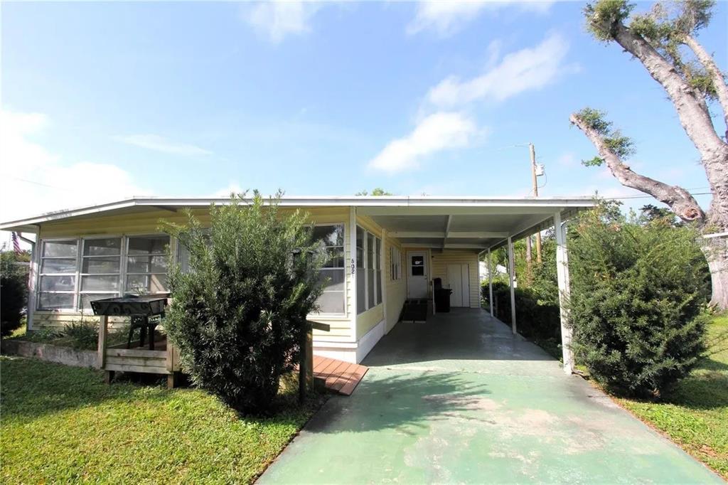 A yellow single-story mobile home features a carport, a front porch, and a grassy yard — 6021 RIDGEWOOD DRIVE, ZEPHYRHILLS, FL