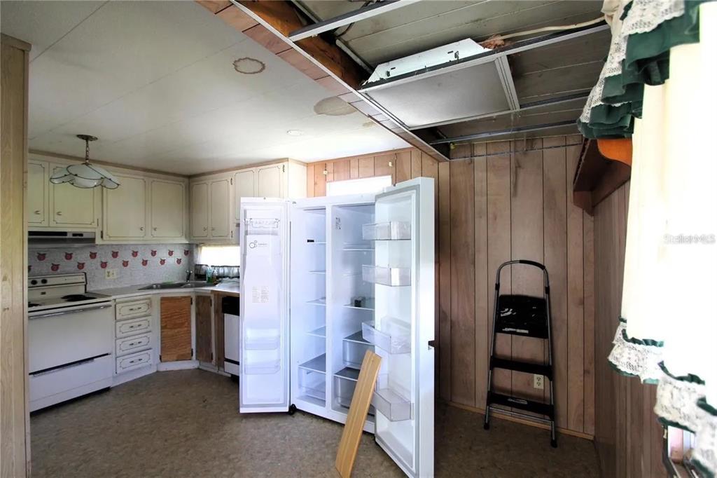 A kitchen with wood-paneled walls, white cabinets, a white refrigerator, and an exposed ceiling grid — 6021 RIDGEWOOD DRIVE, ZEPHYRHILLS, FL