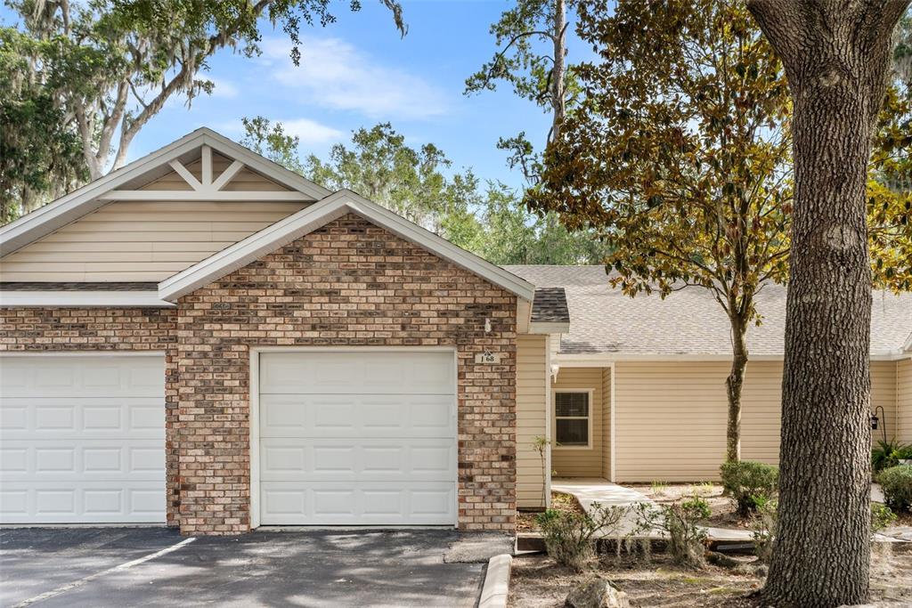 A tan house with a brick facade, two white garage doors, and a paved driveway — 4700 SW ARCHER ROAD UNIT 68, GAINESVILLE, FL