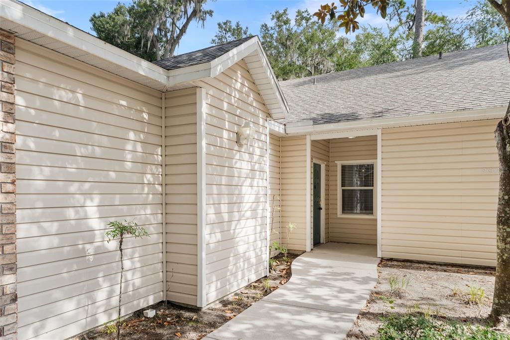 The exterior of a tan, vinyl-sided house features a concrete walkway leading to the front door — 4700 SW ARCHER ROAD UNIT 68, GAINESVILLE, FL