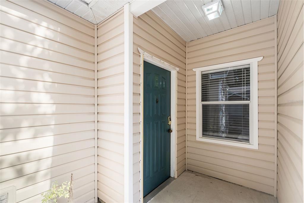 A covered entryway features beige vinyl siding, a teal front door, and a single window — 4700 SW ARCHER ROAD UNIT 68, GAINESVILLE, FL