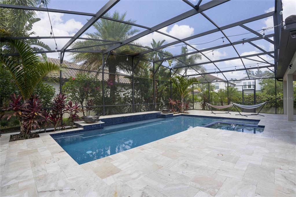 A screened-in pool patio features a rectangular swimming pool, a spa, and stone tile flooring — 8414 VIVARO ISLE WAY, WINDERMERE, FL
