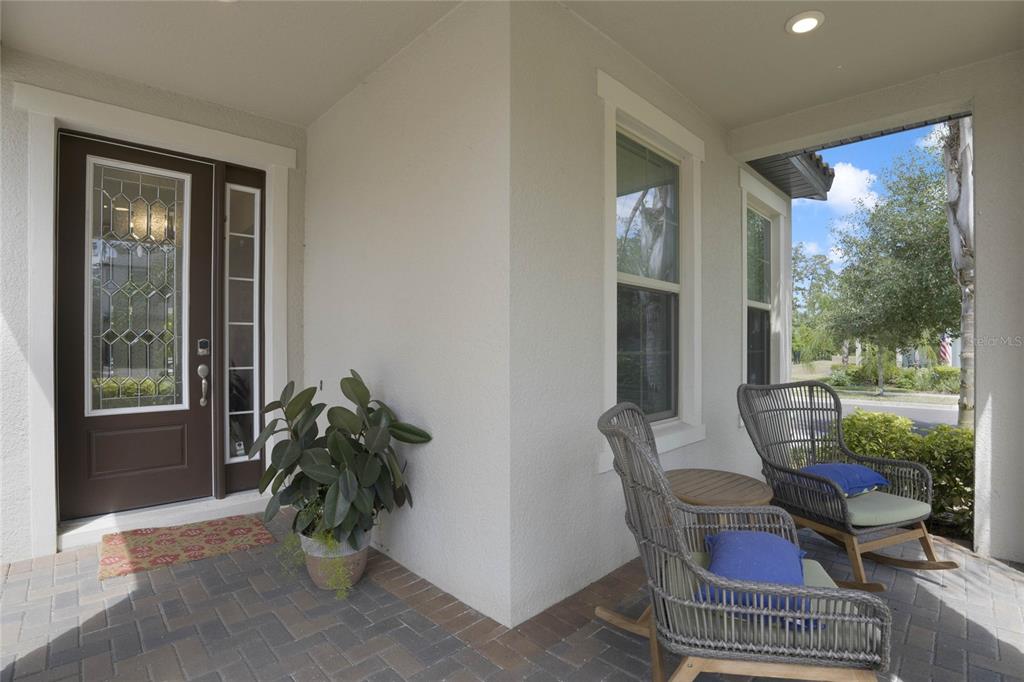 A covered front porch features a dark brown door, two wicker rocking chairs, and pavers — 8414 VIVARO ISLE WAY, WINDERMERE, FL