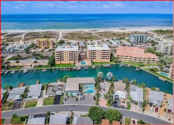An aerial view shows a coastal residential area with apartment buildings, a canal, and beach — 11440 1ST STREET E UNIT 6, TREASURE ISLAND, FL