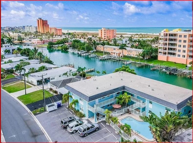 An aerial view shows a blue apartment building with a pool next to a canal — 11440 1ST STREET E UNIT 6, TREASURE ISLAND, FL