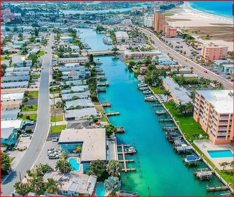 An aerial view shows a canal lined with residential buildings, boat docks, and swimming pools — 11440 1ST STREET E UNIT 6, TREASURE ISLAND, FL