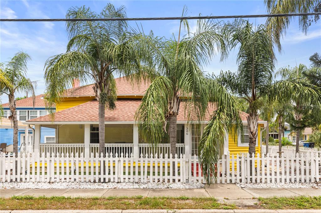 A yellow house with a screened-in porch and white picket fence behind palm trees — 306 MARSHALL STREET, CLEARWATER, FL