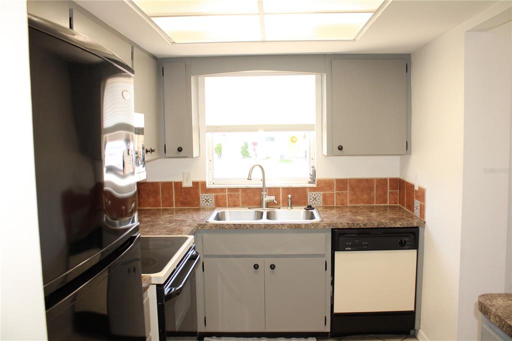 A kitchen features gray cabinets, a double sink, a black refrigerator, and brown tile backsplash — 5062 LIVE OAK CIRCLE UNIT 5026, BRADENTON, FL