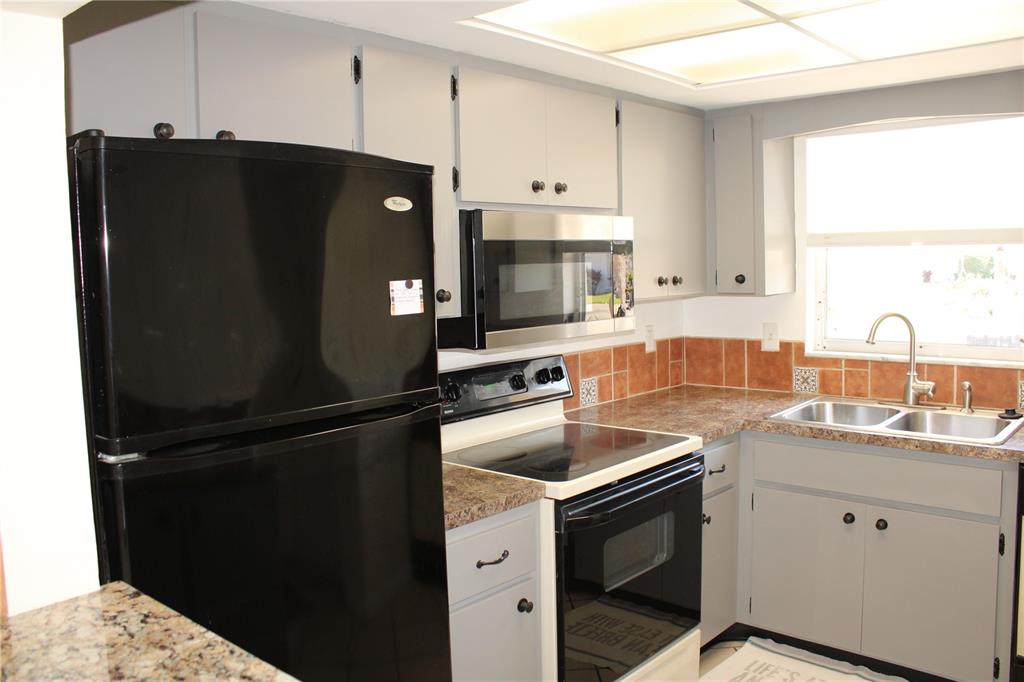 A kitchen features grey cabinets, black appliances, a stainless steel microwave, and brown tile backsplash — 5062 LIVE OAK CIRCLE UNIT 5026, BRADENTON, FL