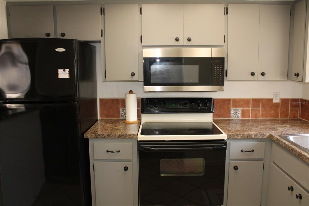 A kitchen features gray cabinets, a black refrigerator, a black stove, and a microwave — 5062 LIVE OAK CIRCLE UNIT 5026, BRADENTON, FL