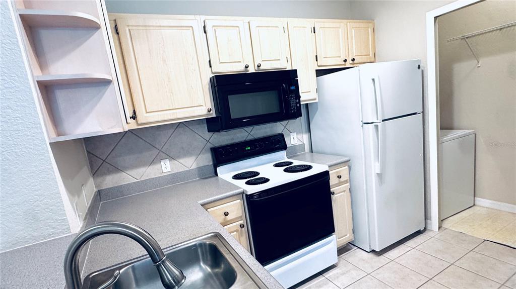 A kitchen features light wood cabinets, a black microwave and stove, and a white refrigerator — 1375 LAKE SHADOW CIRCLE UNIT 11203, MAITLAND, FL