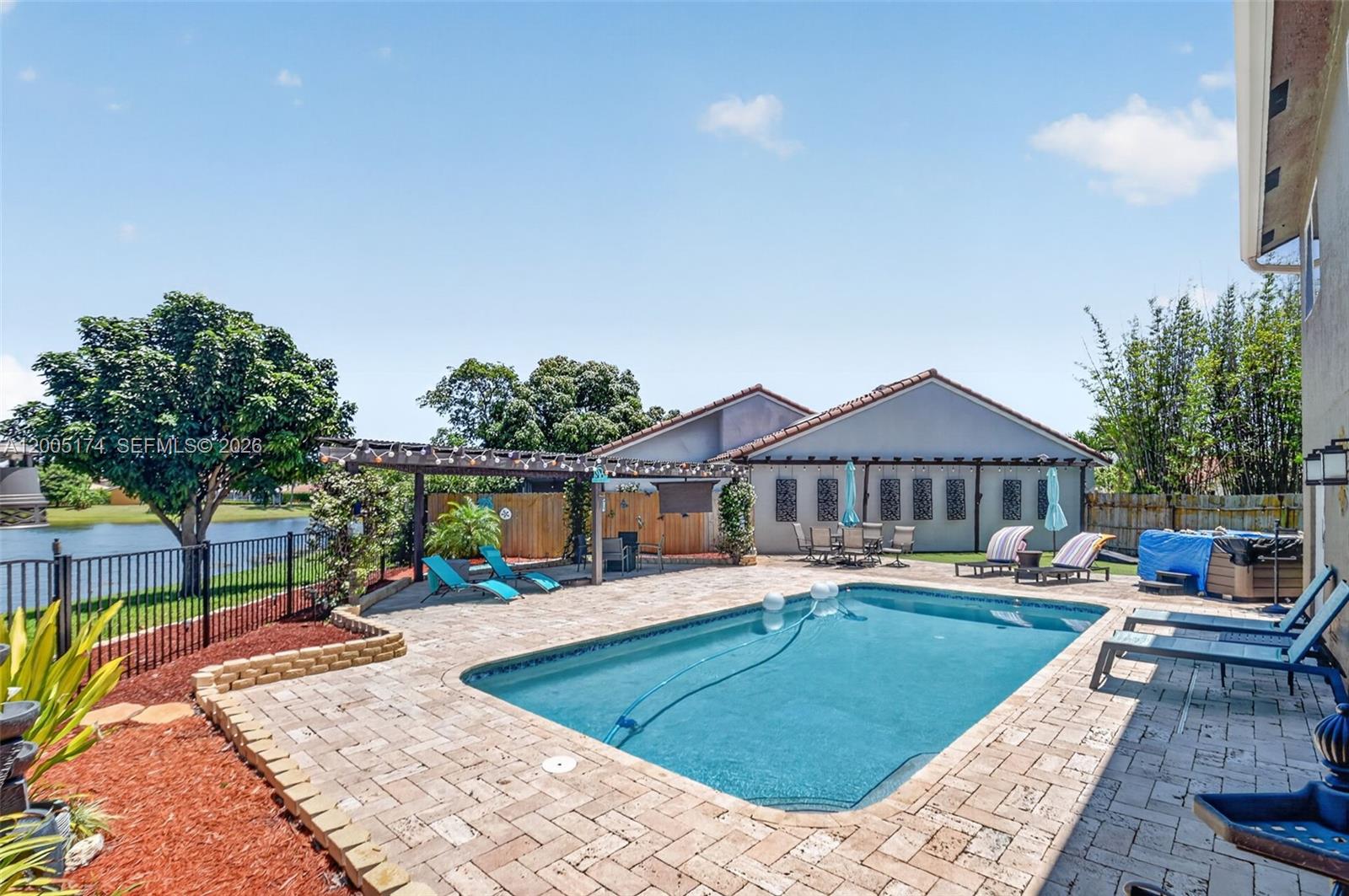 A backyard features a swimming pool, a paved patio, a pergola, and a lake view — 6269 Country Fair Circle, Boynton Beach FL 33437, BOYNTON BEACH, FL