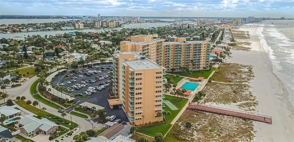 An aerial view shows a tall, tan beachfront condominium complex with a pool and parking lot — 880 MANDALAY AVENUE UNIT S804, CLEARWATER BEACH, FL