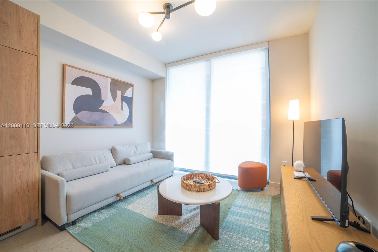 A modern living room features a light-colored sofa, a round coffee table, and a television — 11 NE 6TH # 1104, Miami FL 33132, MIAMI, FL