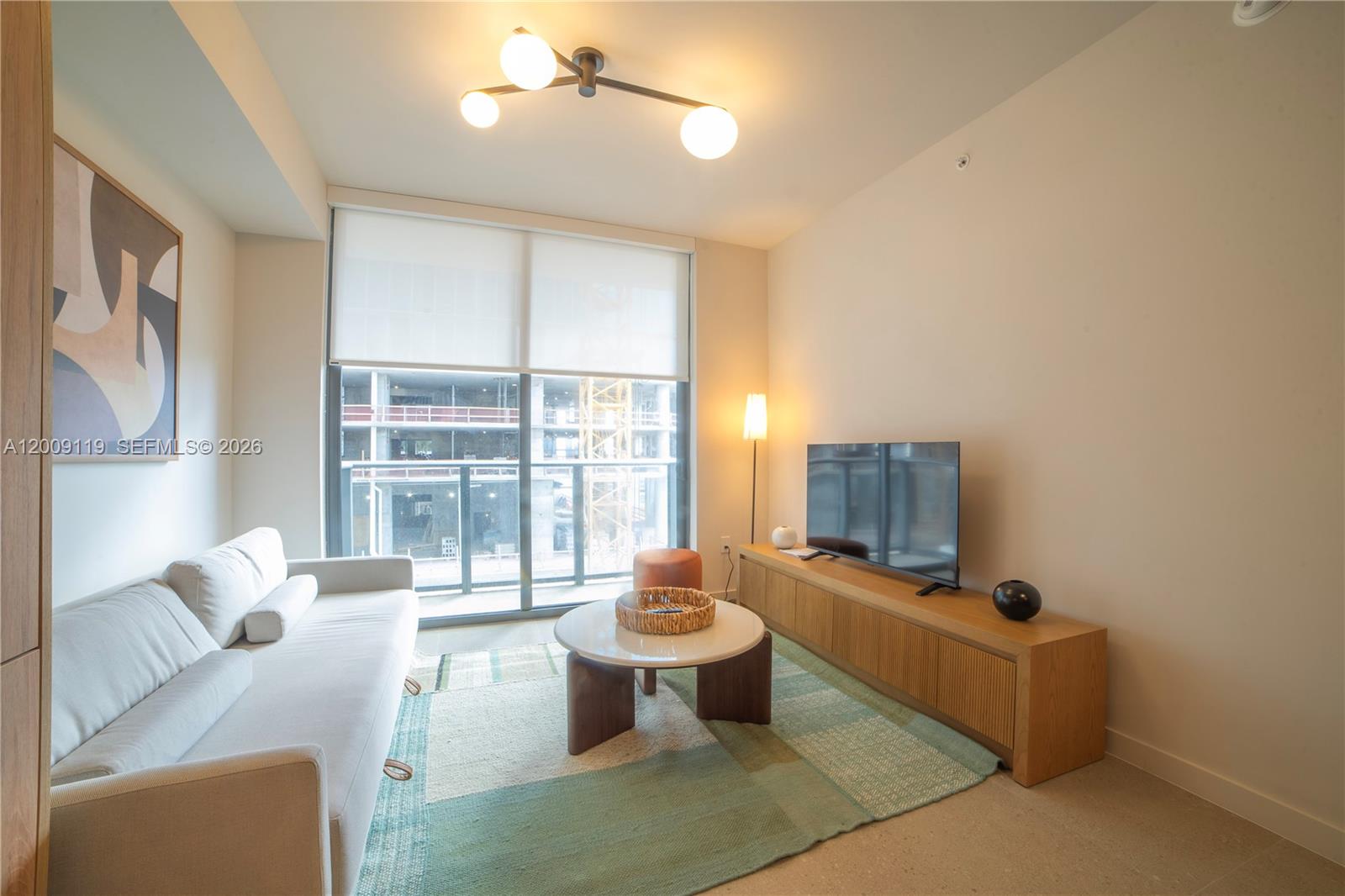A modern living room features a white sofa, a round coffee table, and a television — 11 NE 6TH # 1104, Miami FL 33132, MIAMI, FL