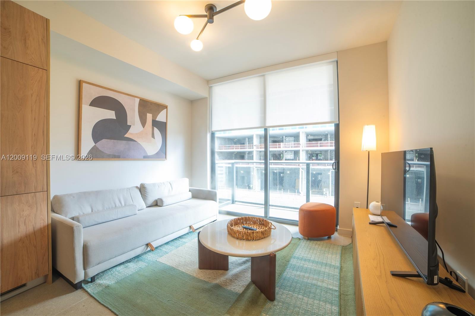 A living room features a light-colored sofa, a round coffee table, and a balcony view — 11 NE 6TH # 1104, Miami FL 33132, MIAMI, FL