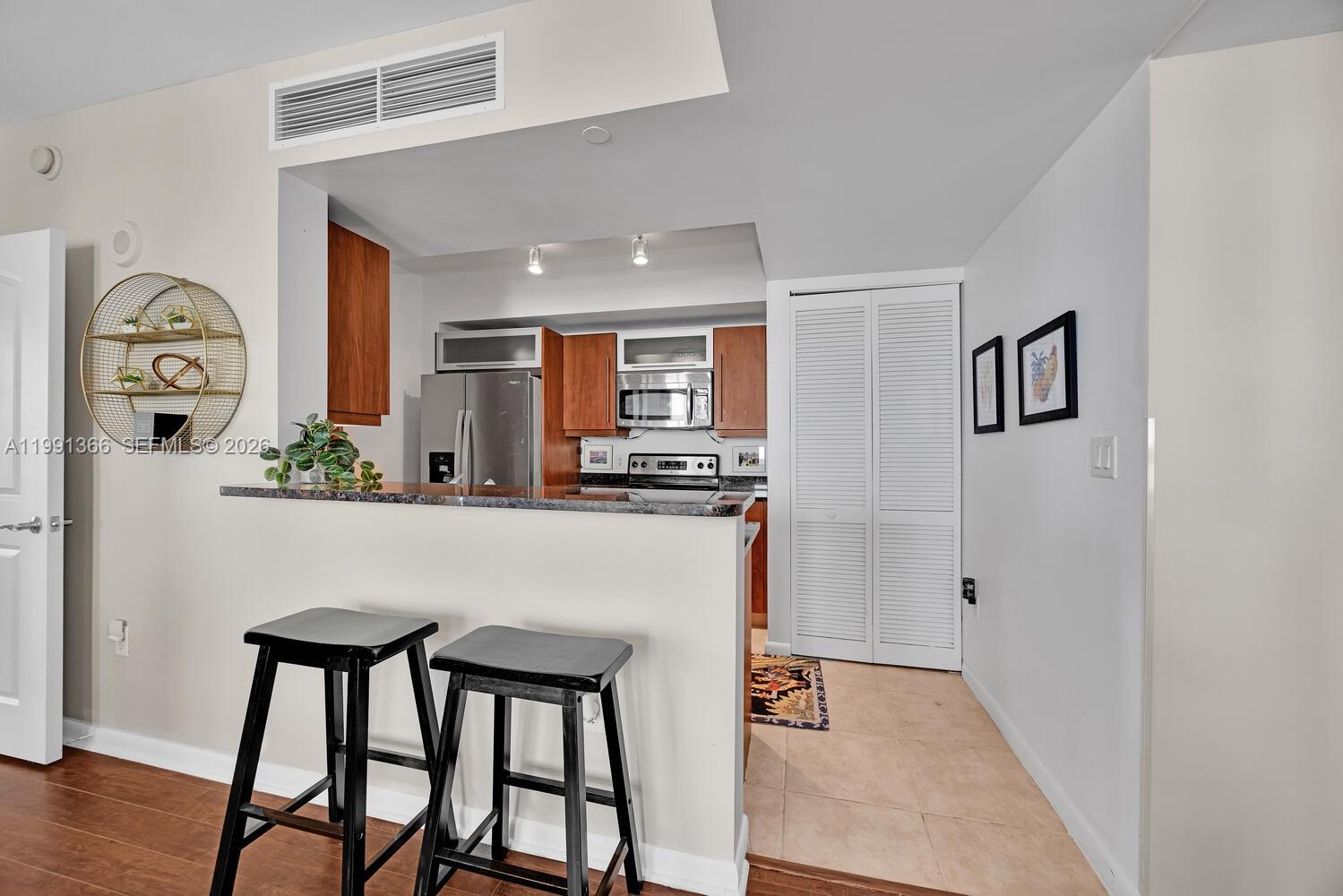 A kitchen with wood cabinets, stainless steel appliances, and a breakfast bar with two stools — 7350 SW 89th St # 1511S, Miami FL 33156, MIAMI, FL