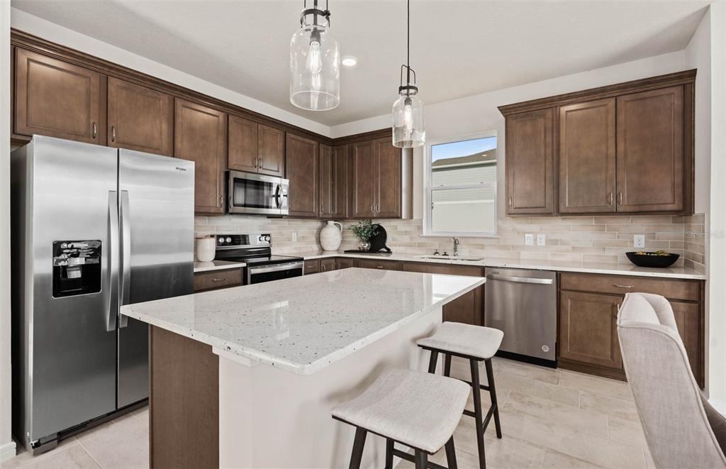 A kitchen features dark wood cabinets, stainless steel appliances, a granite island, and pendant lighting — 1440 HAMILTON WAY, LAKE ALFRED, FL