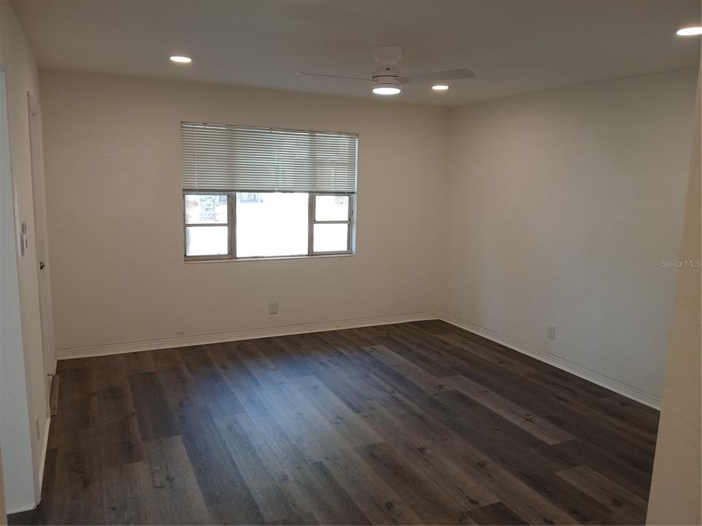 An empty room features white walls, dark wood-look flooring, a ceiling fan, and a window — 921 WINCHESTER STREET, DAYTONA BEACH, FL