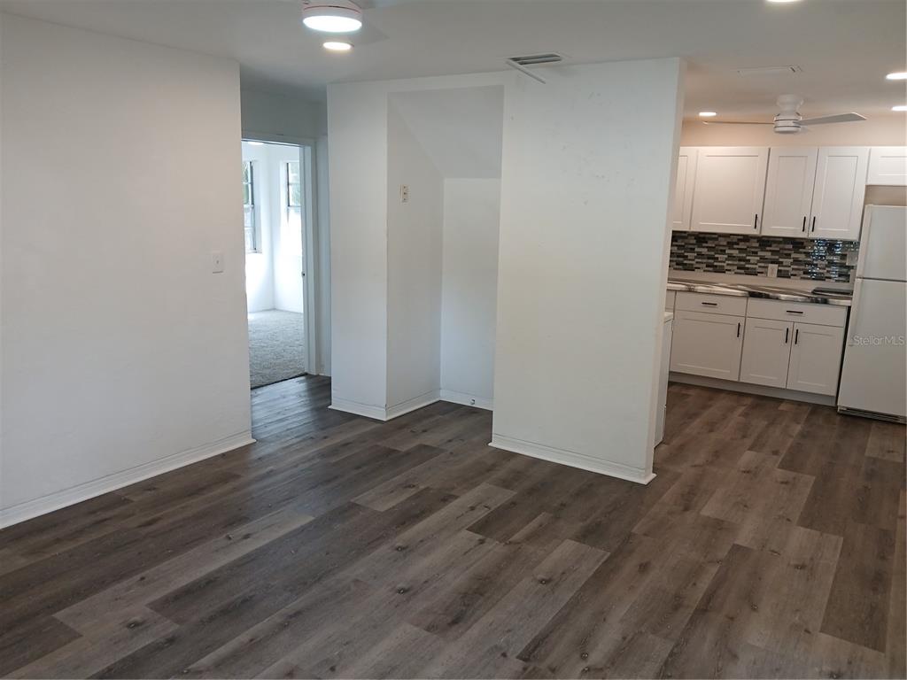 A room with wood-look flooring leads to a kitchen with white cabinets and a tiled backsplash — 921 WINCHESTER STREET, DAYTONA BEACH, FL