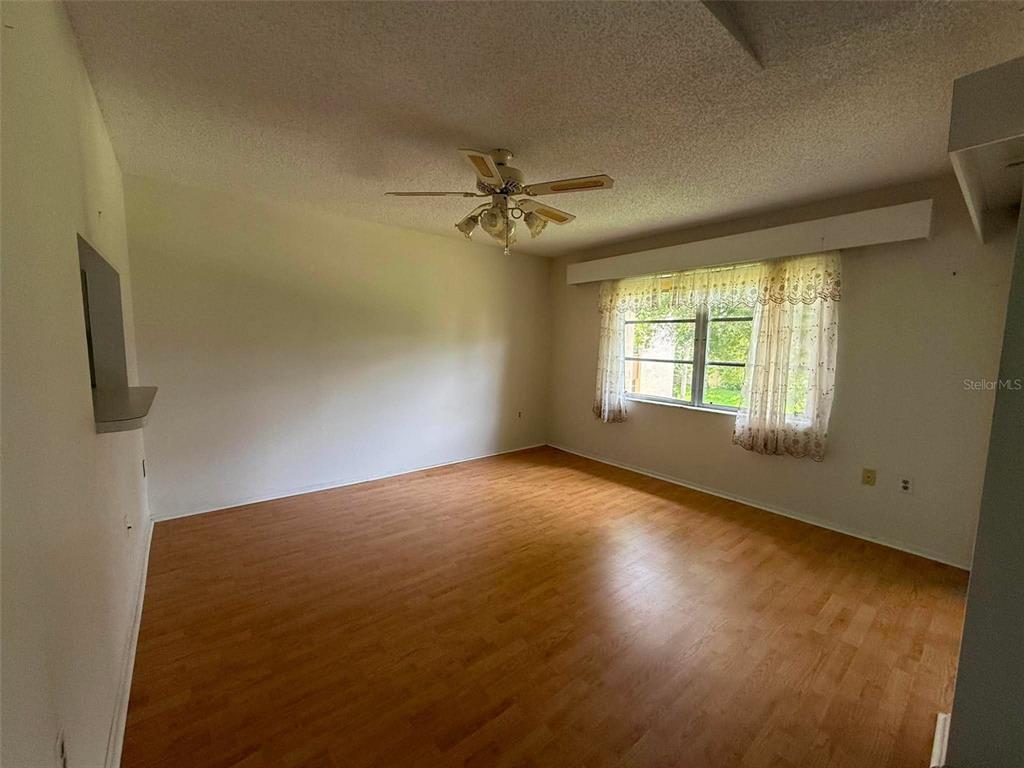 An empty room features light wood-look flooring, a ceiling fan, and a large window with curtains — 2536 CLUBHOUSE CIRCLE UNIT 202, SARASOTA, FL