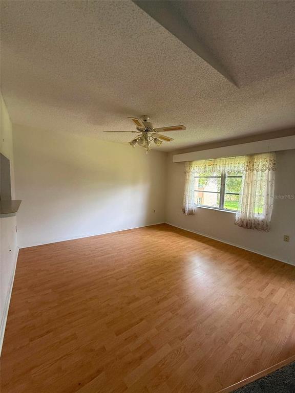 A living room with light wood-look flooring, a ceiling fan, and a window with curtains — 2536 CLUBHOUSE CIRCLE UNIT 202, SARASOTA, FL