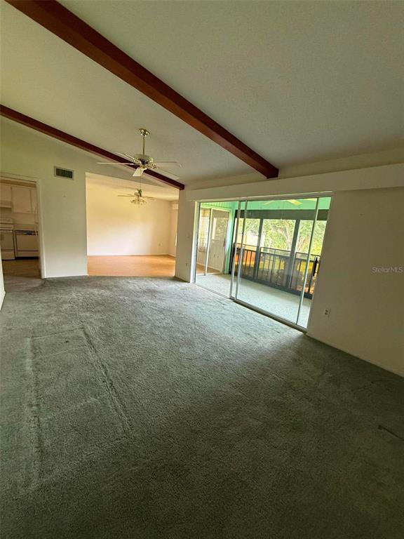 A living room features green carpeting, exposed ceiling beams, and a sliding glass door — 2536 CLUBHOUSE CIRCLE UNIT 202, SARASOTA, FL