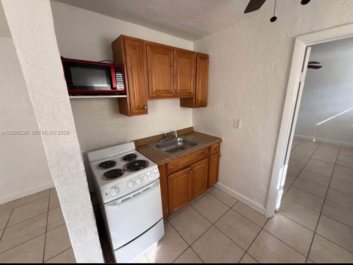 A small kitchen features wooden cabinets, a white stove, a sink, and a microwave — 5731 Flagler St # 1, Hollywood FL 33023, HOLLYWOOD, FL
