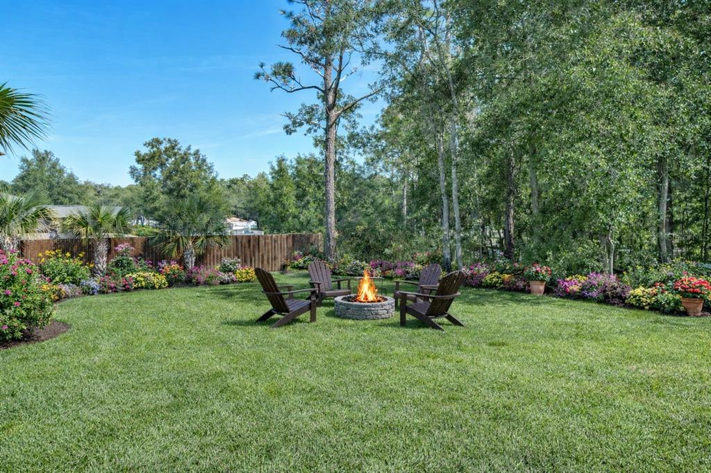 A backyard features a stone fire pit surrounded by four wooden chairs on a lawn — 12805 SW 64TH LANE, OCALA, FL