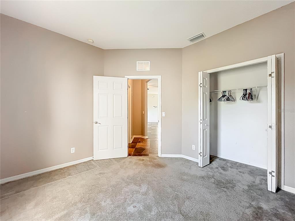 An empty bedroom features beige walls, gray carpeting, a closet, and an open doorway — 12805 SW 64TH LANE, OCALA, FL