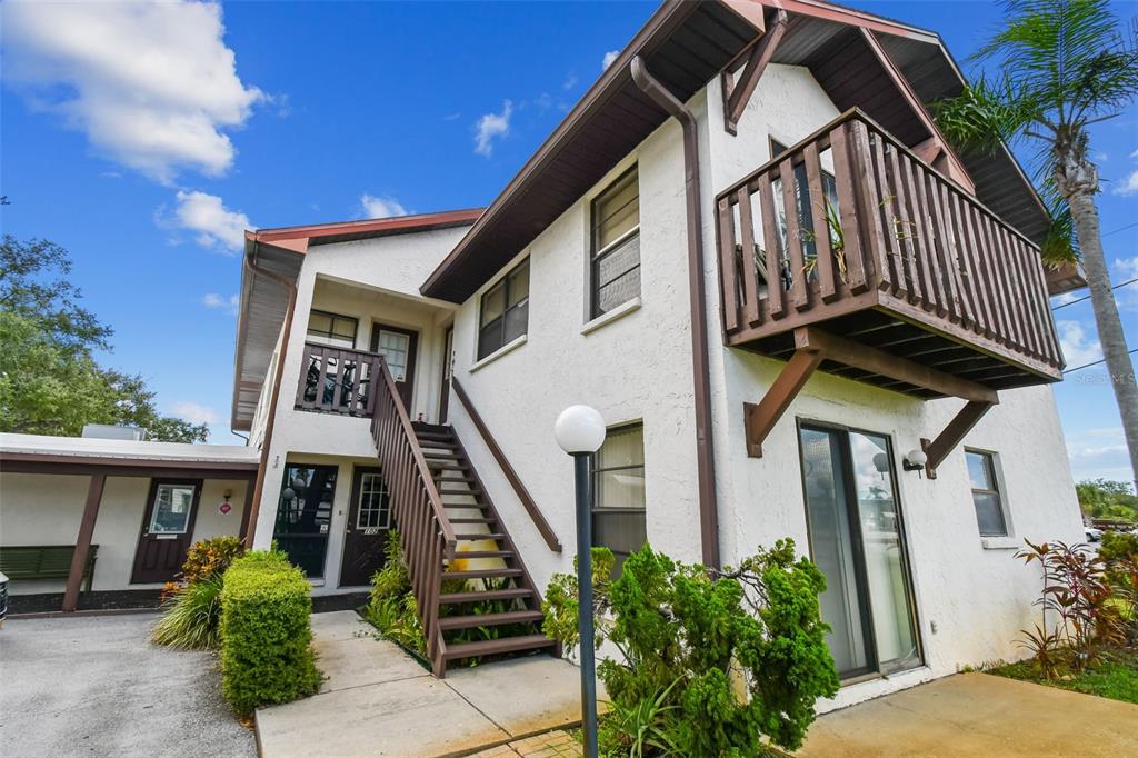 A two-story stucco building features an exterior staircase, a wooden balcony, and a covered carport — 8423 SEMINOLE BLVD UNIT 203, SEMINOLE, FL