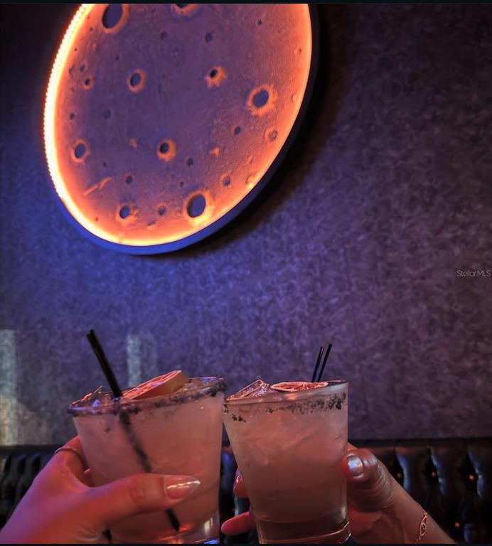 Two cocktails are held up in front of a wall featuring a glowing moon-shaped light — DOWNTOWN BAR, ORLANDO, FL