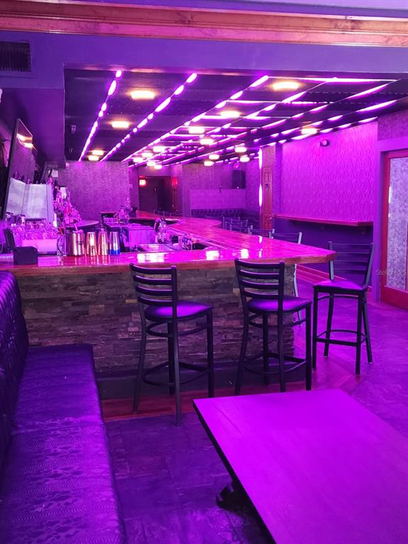 A bar area features a stone-faced counter, high-top stools, and vibrant purple ceiling lighting — DOWNTOWN BAR, ORLANDO, FL