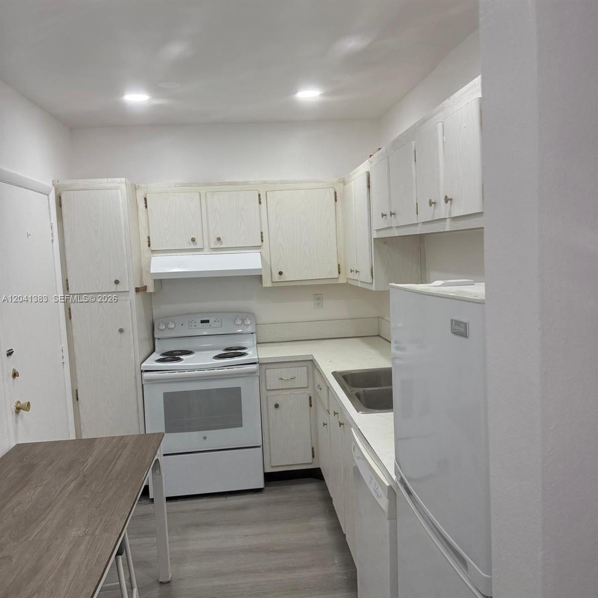 A galley kitchen features white cabinets, white appliances, and light-colored wood-look flooring — 9159 SW 77th Ave # 211, Miami FL 33156, MIAMI, FL