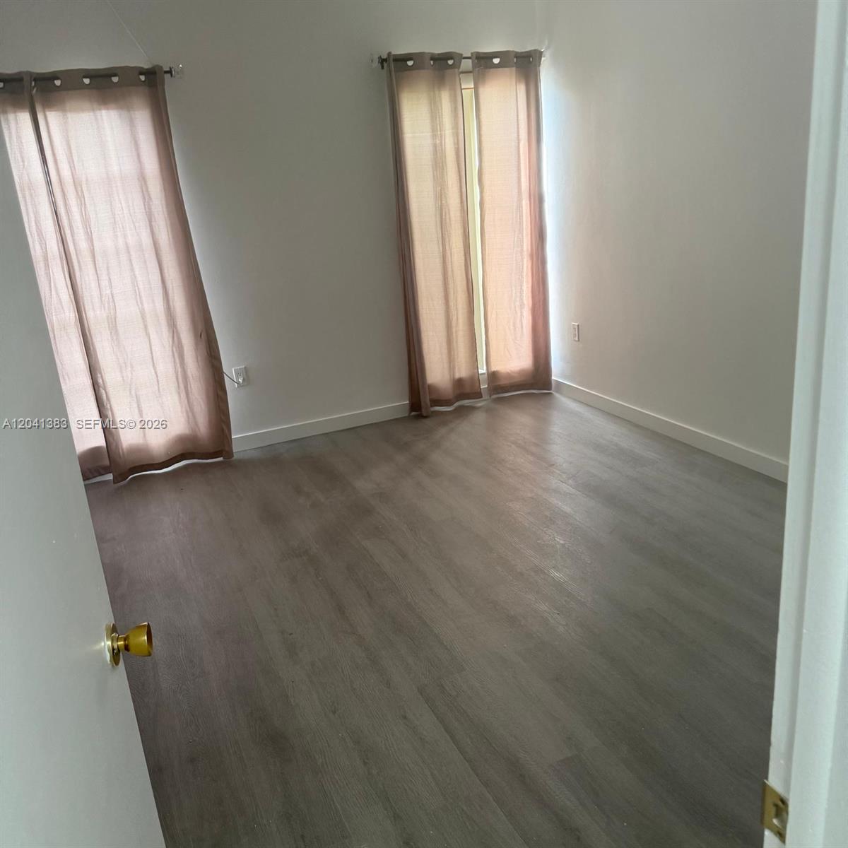 An empty bedroom features light-colored walls, wood-look flooring, and two windows with brown curtains — 9159 SW 77th Ave # 211, Miami FL 33156, MIAMI, FL