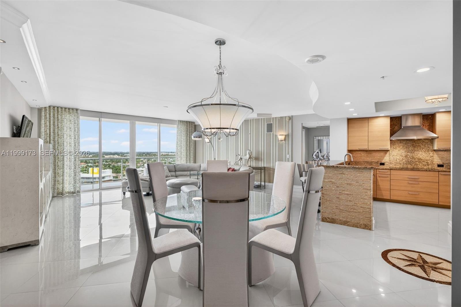 A dining area with a glass table and chairs sits before an open kitchen and balcony — 1 N Ocean Blvd # 1408, Pompano Beach FL 33062, POMPANO BEACH, FL