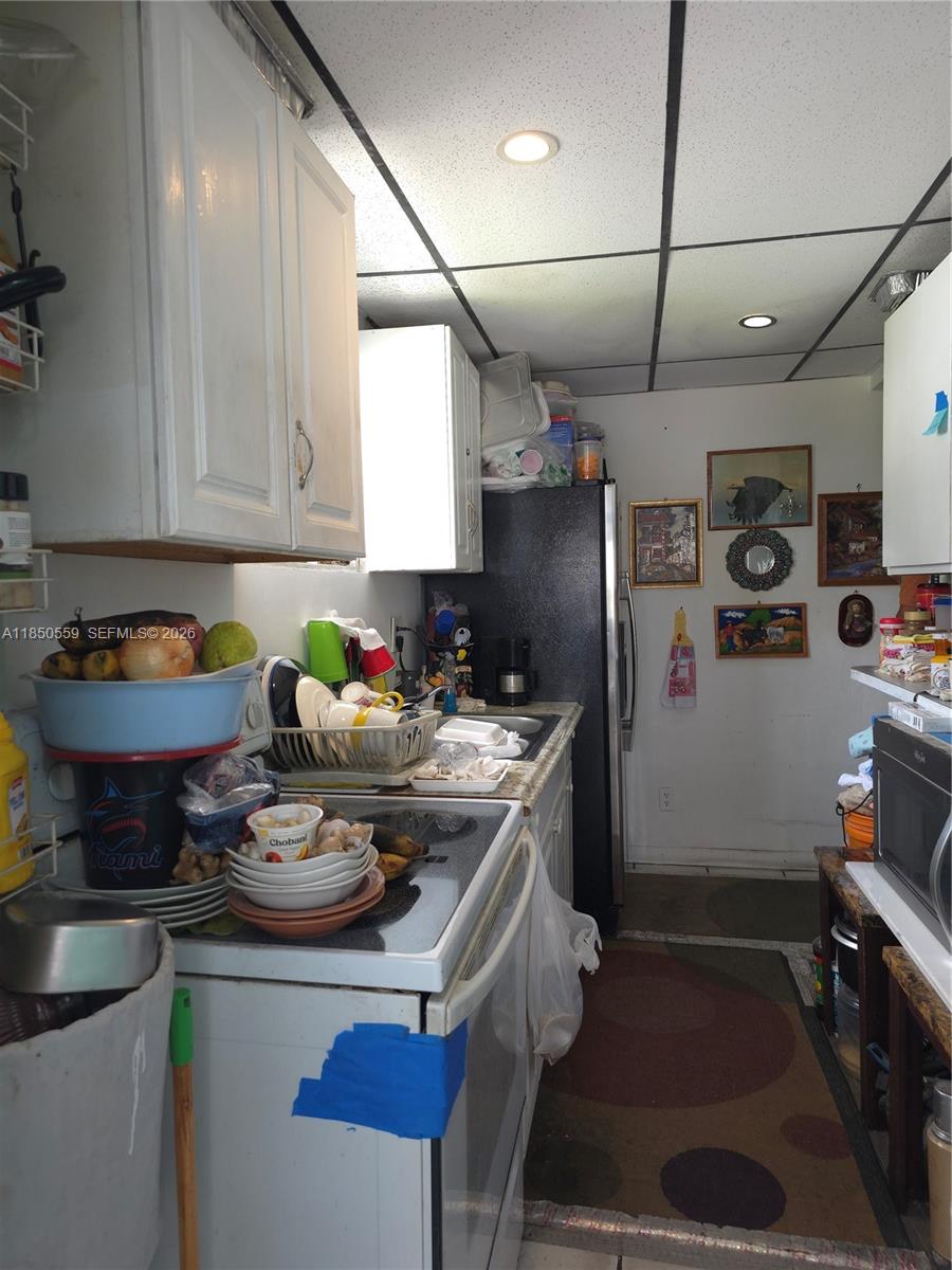 A narrow kitchen features white cabinets, a black refrigerator, and a stove with cluttered countertops — 163 NW 18th Ct, Miami FL 33125, MIAMI, FL