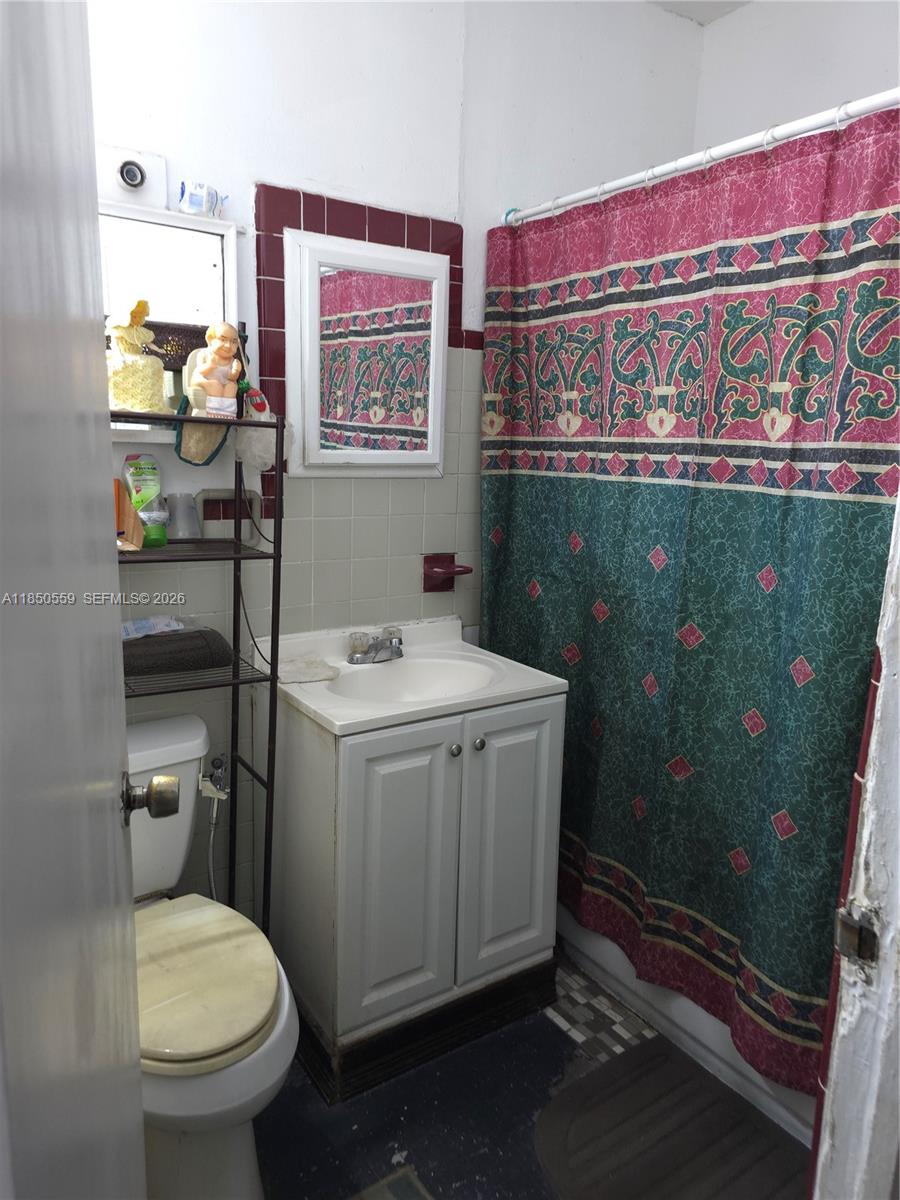 A small bathroom features a white vanity, a toilet, and a patterned shower curtain — 163 NW 18th Ct, Miami FL 33125, MIAMI, FL