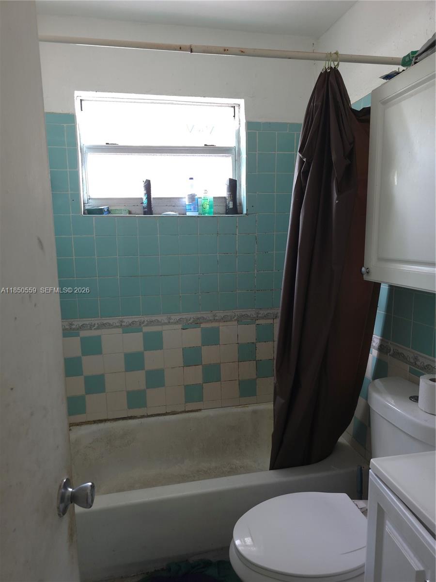 A bathroom features a bathtub with a brown curtain and blue and white tiled walls — 163 NW 18th Ct, Miami FL 33125, MIAMI, FL