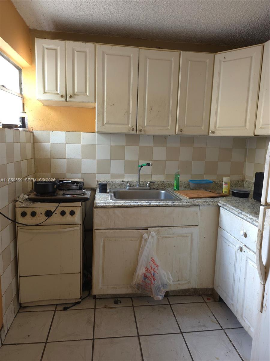 A small kitchen features white cabinets, a stainless steel sink, and a compact electric stove — 163 NW 18th Ct, Miami FL 33125, MIAMI, FL