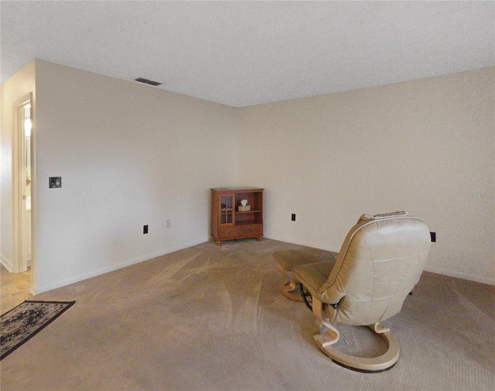 A beige carpeted room features a tan leather recliner and a small wooden cabinet — 504 SILVER COURSE UNIT A, OCALA, FL