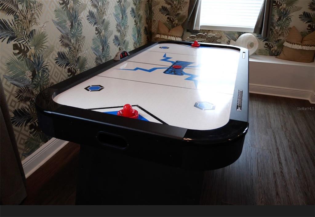 An air hockey table sits in a room with patterned wallpaper and dark wood flooring — 448 SOUTHFIELD STREET, KISSIMMEE, FL