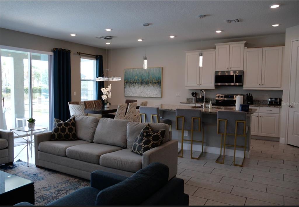 An open-concept living room and kitchen featuring light gray furniture, white cabinetry, and tile flooring — 448 SOUTHFIELD STREET, KISSIMMEE, FL