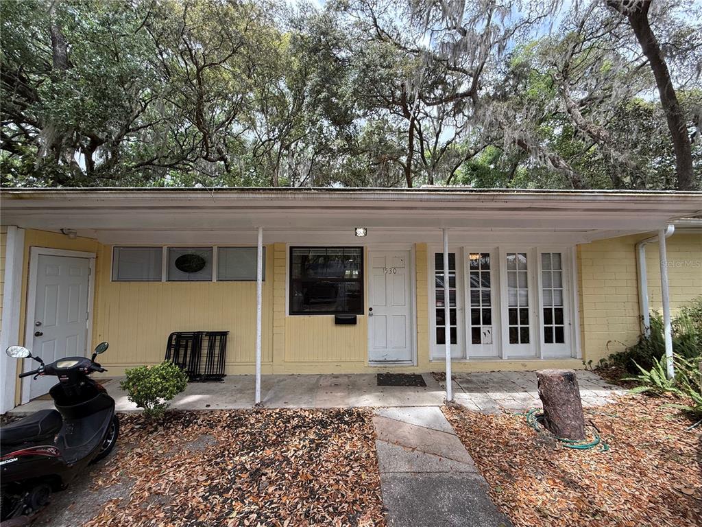 The exterior of a yellow, single-story house features a covered porch and a scooter — 1530 NW 6TH AVENUE, GAINESVILLE, FL