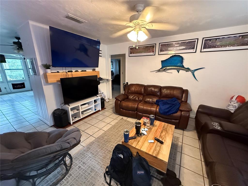 A living room features a leather sofa, a wooden coffee table, and two televisions — 1530 NW 6TH AVENUE, GAINESVILLE, FL